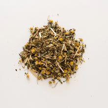 Load image into Gallery viewer, A small pile of Serenity Tea, consisting of dried chamomile flowers and green herb leaves and stems, lies scattered on a plain white surface. This organic infusion showcases a rustic appearance with its blend of yellow flowers and green-brown stems, making it the perfect choice for those seeking calmness and serenity to aid sleep.