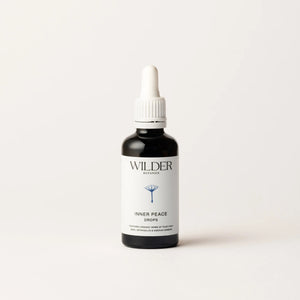 A black dropper bottle with a white label stands against a light background. The label reads "Wilder Botanics" at the top and "Inner Peace Drops" below, featuring a simple tree illustration. Infused with Tulsi, the bottle has a white dropper cap.