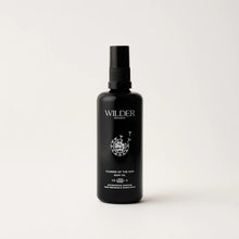 Load image into Gallery viewer, A sleek, black bottle of &quot;Flower of the Sun Body Oil&quot; with a convenient spray nozzle. The label boasts a delicate floral illustration and emphasizes the inclusion of 13 botanicals such as Calendula oil, which are designed to nourish and enhance skin hydration. The bottle is photographed against a simple white background.