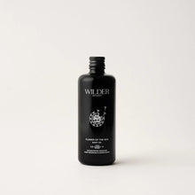 Load image into Gallery viewer, A minimalist black bottle of Flower of the Sun Body Oil from Wilder Botanics, featuring a white floral design and text. Enriched with Calendula oil for ultimate skin hydration, the bottle has a screw cap and stands against a plain, light-gray background. Its 138ml volume is indicated at the bottom.