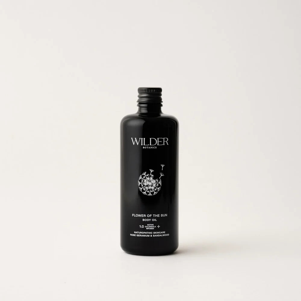 A minimalist black bottle of Flower of the Sun Body Oil from Wilder Botanics, featuring a white floral design and text. Enriched with Calendula oil for ultimate skin hydration, the bottle has a screw cap and stands against a plain, light-gray background. Its 138ml volume is indicated at the bottom.