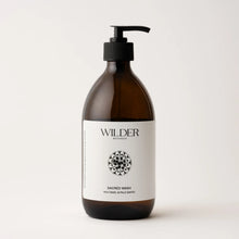 Load image into Gallery viewer, A brown bottle with a black pump dispenser features a minimalist label reading &quot;Wilder Botanics&quot; at the top. Below is a circular decorative emblem and the text &quot;Sacred Wash - Holy Basil &amp; Palo Santo.&quot; This hand and body wash, named Sacred Wash, includes Tulsi extract and Palo Santo extract. The bottle sits on a white background.