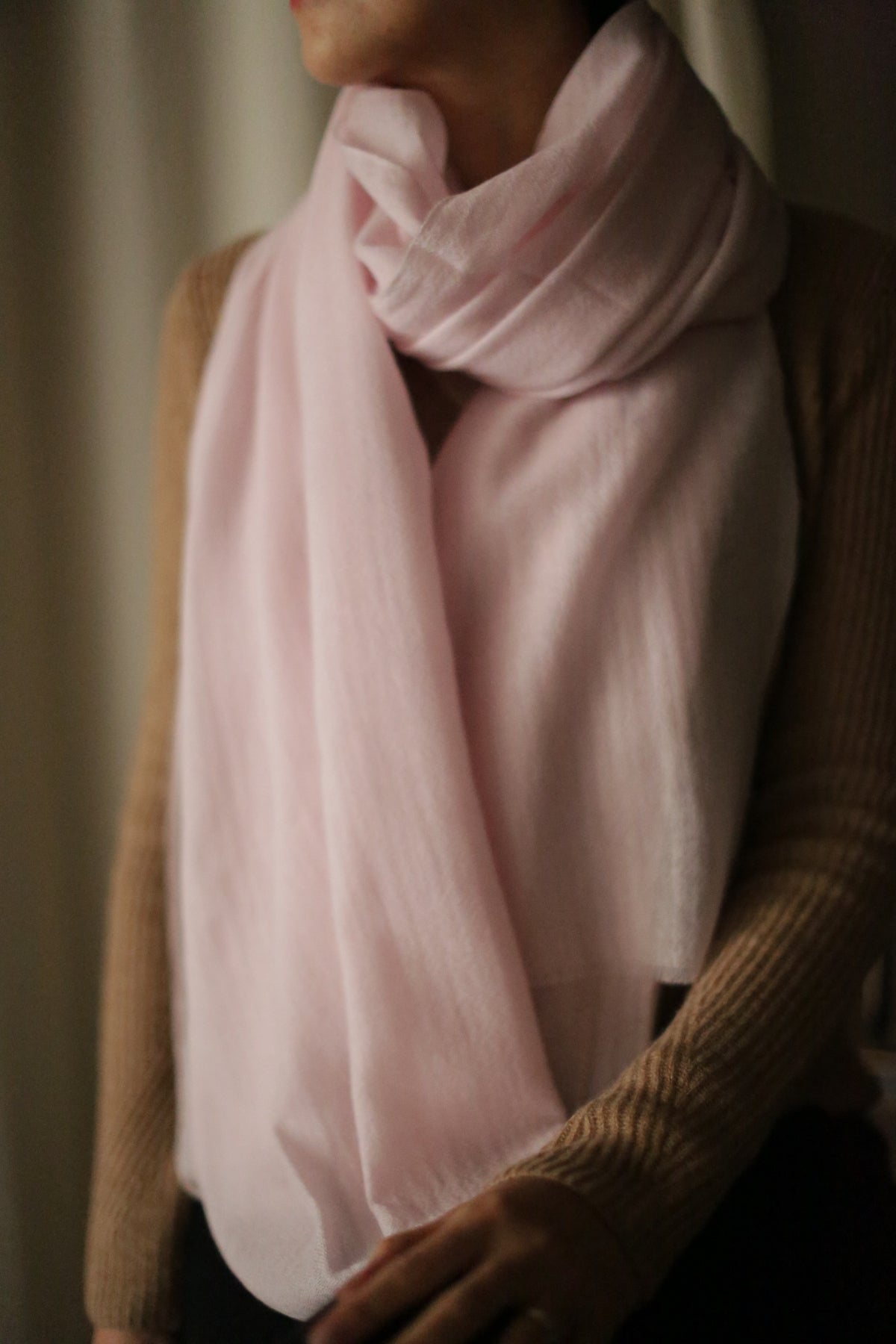 A person wearing the Tissue Weight Cashmere Scarf in pink is draped over their shoulders and neck, paired with a beige, long-sleeved sweater. Their face is partially out of frame and turned to the side.