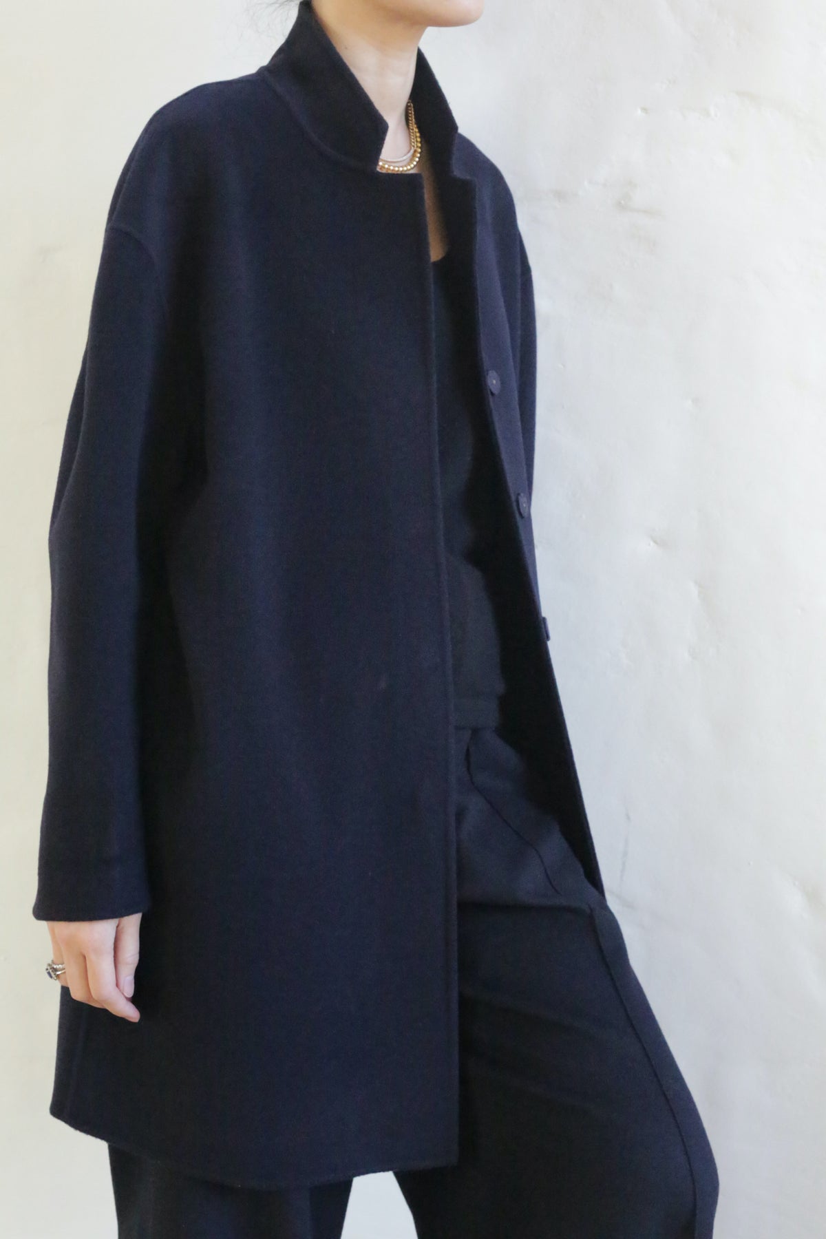 A person wears the Bamford Double-face Cashmere in navy—an oversized blazer paired with matching trousers—standing by a light wall, their face partially out of frame and one hand resting at their side.