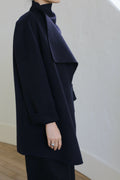 A person wearing the Winston Double-face Cashmere coat in navy stands by a light wall. Only their lower face and upper body are visible, with a relaxed hand at their side revealing a silver ring.
