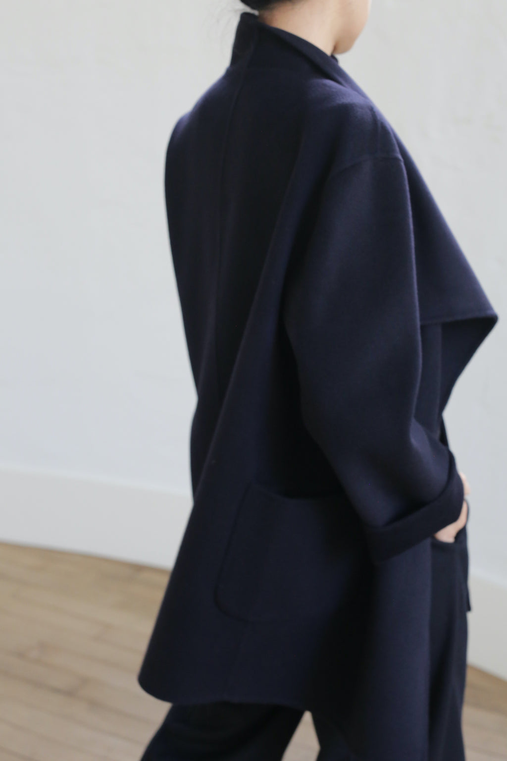 A person wears the Winston Double-face Cashmere jacket in Navy, standing in a minimal, light-toned room with wooden floors, their hand in a pocket and face not visible.