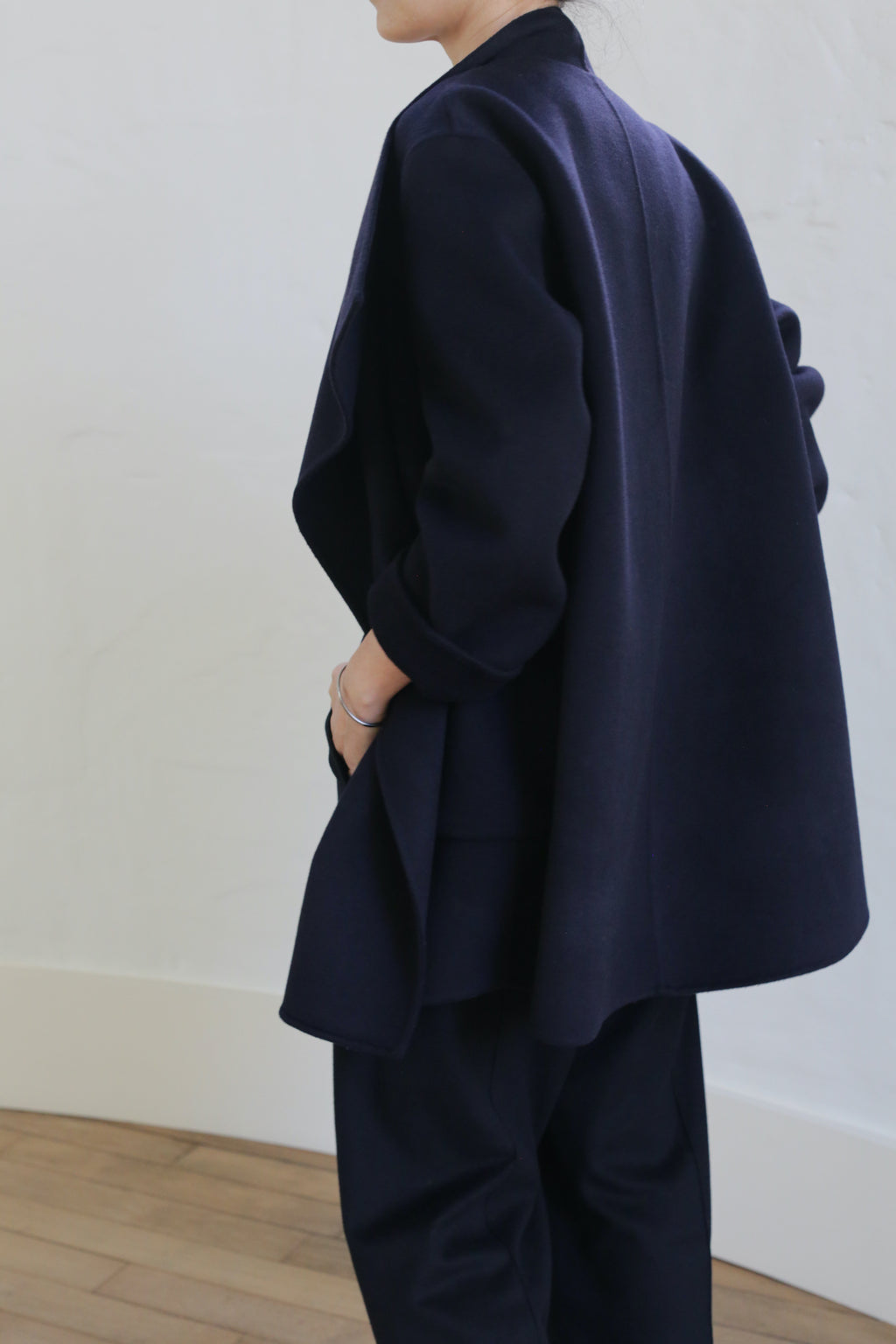A person in the Winston Double-face Cashmere blazer and matching navy pants stands sideways against a light wall, resting one hand on their hip; their face is partially out of frame.