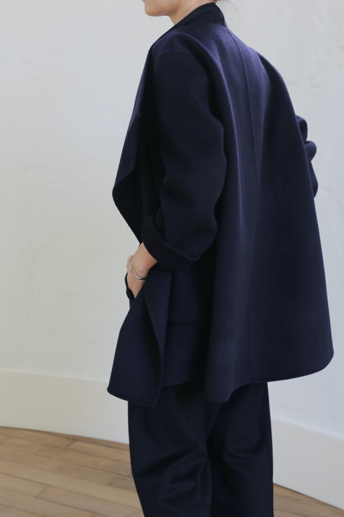 A person in the Winston Double-face Cashmere blazer and matching navy pants stands sideways against a light wall, resting one hand on their hip; their face is partially out of frame.