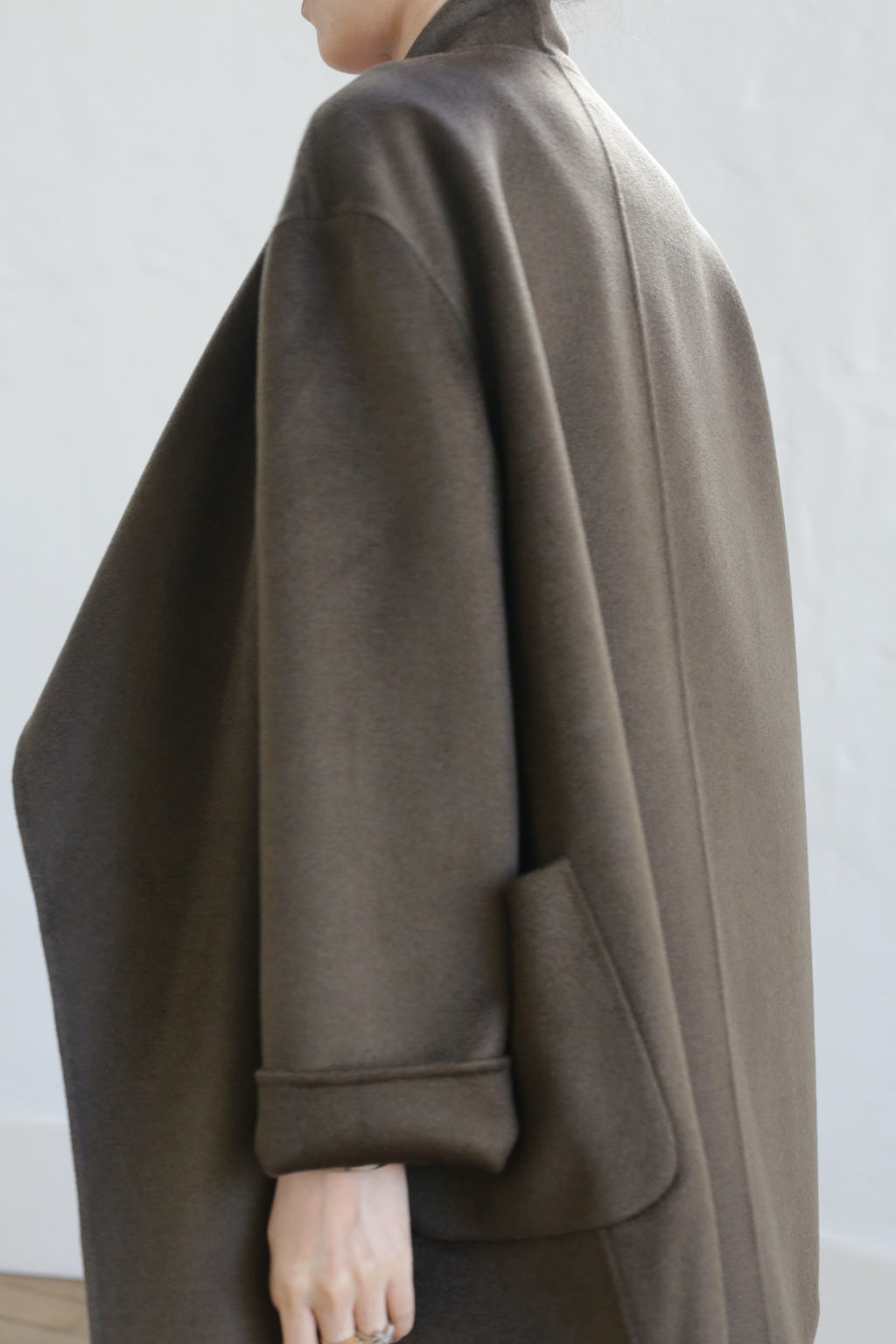 A person wearing the Winston Double-face Cashmere coat in Olive stands against a light background. The image highlights the side and back, showcasing the coat’s oversized fit, wide collar, and graceful drape.