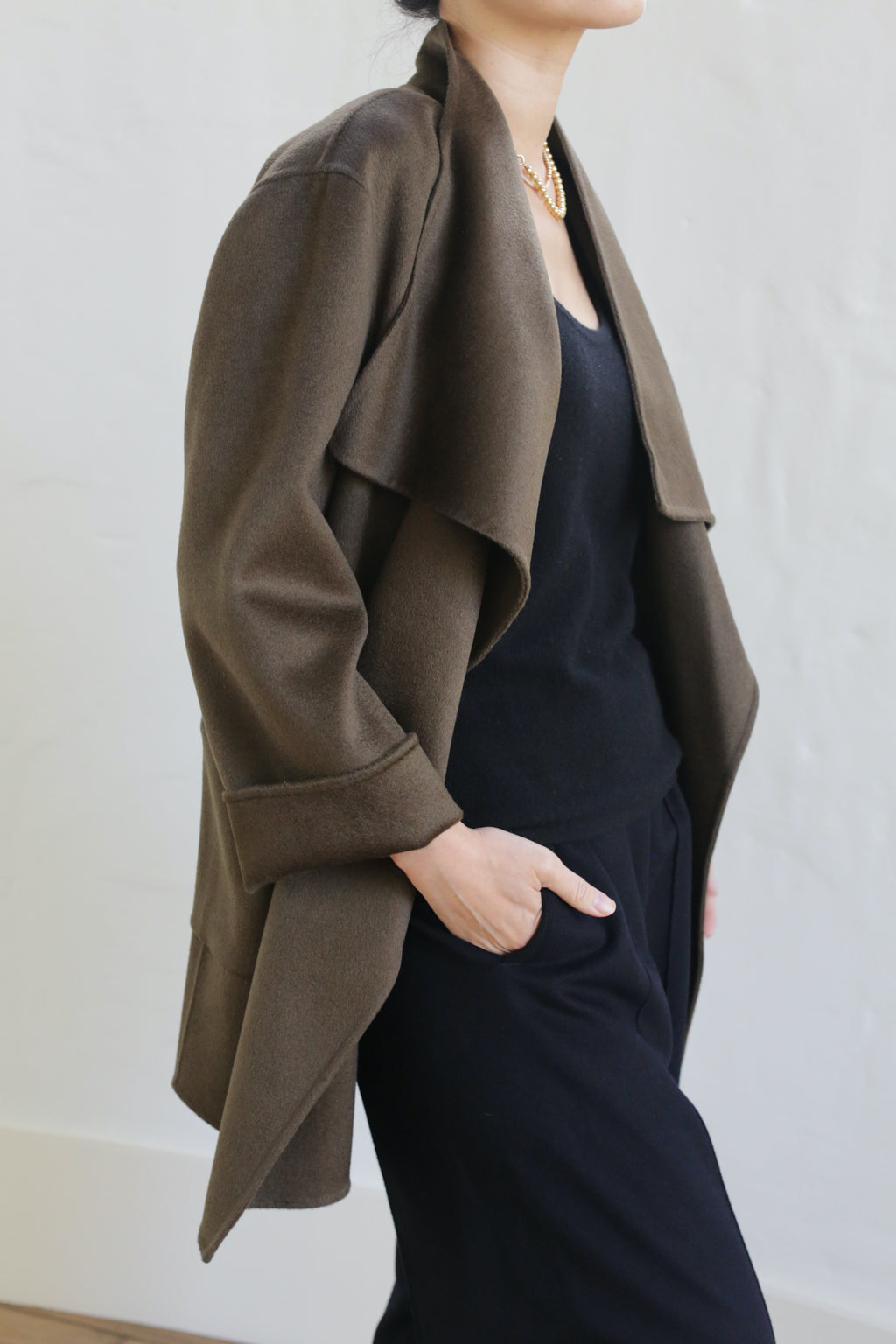 A person wearing the Winston Double-face Cashmere jacket in olive over a black top and pants stands with one hand in their pocket against a plain light background, their face not visible.