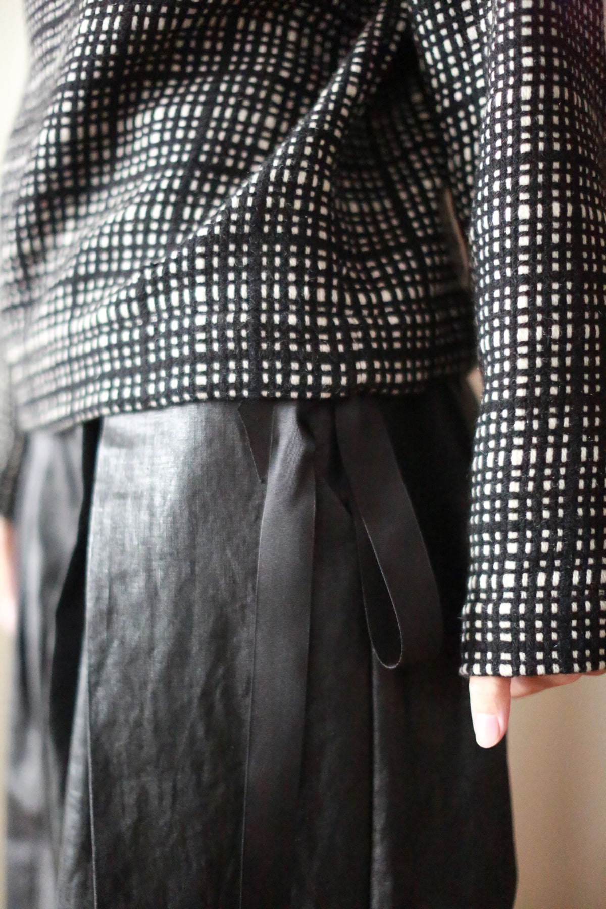 A person in an Alex Hoodie | Plaid, sporting a black and white checkered long-sleeve top paired with black pants featuring a silk ribbon waist. The midsection is highlighted, showcasing the stylish texture and pattern of this handmade outfit from San Francisco.