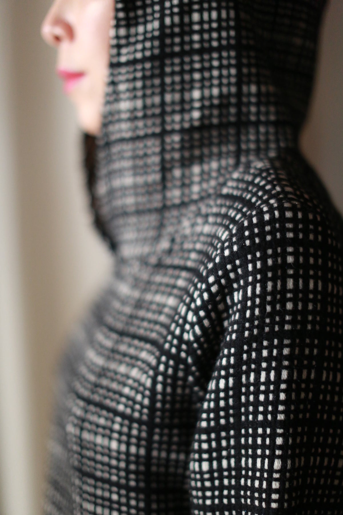 A person is shown in profile wearing the Alex Hoodie | Plaid, handmade in San Francisco. The focus is on the black and white checkered pattern of the hooded jacket, with a blurred background highlighting its unique craftsmanship.