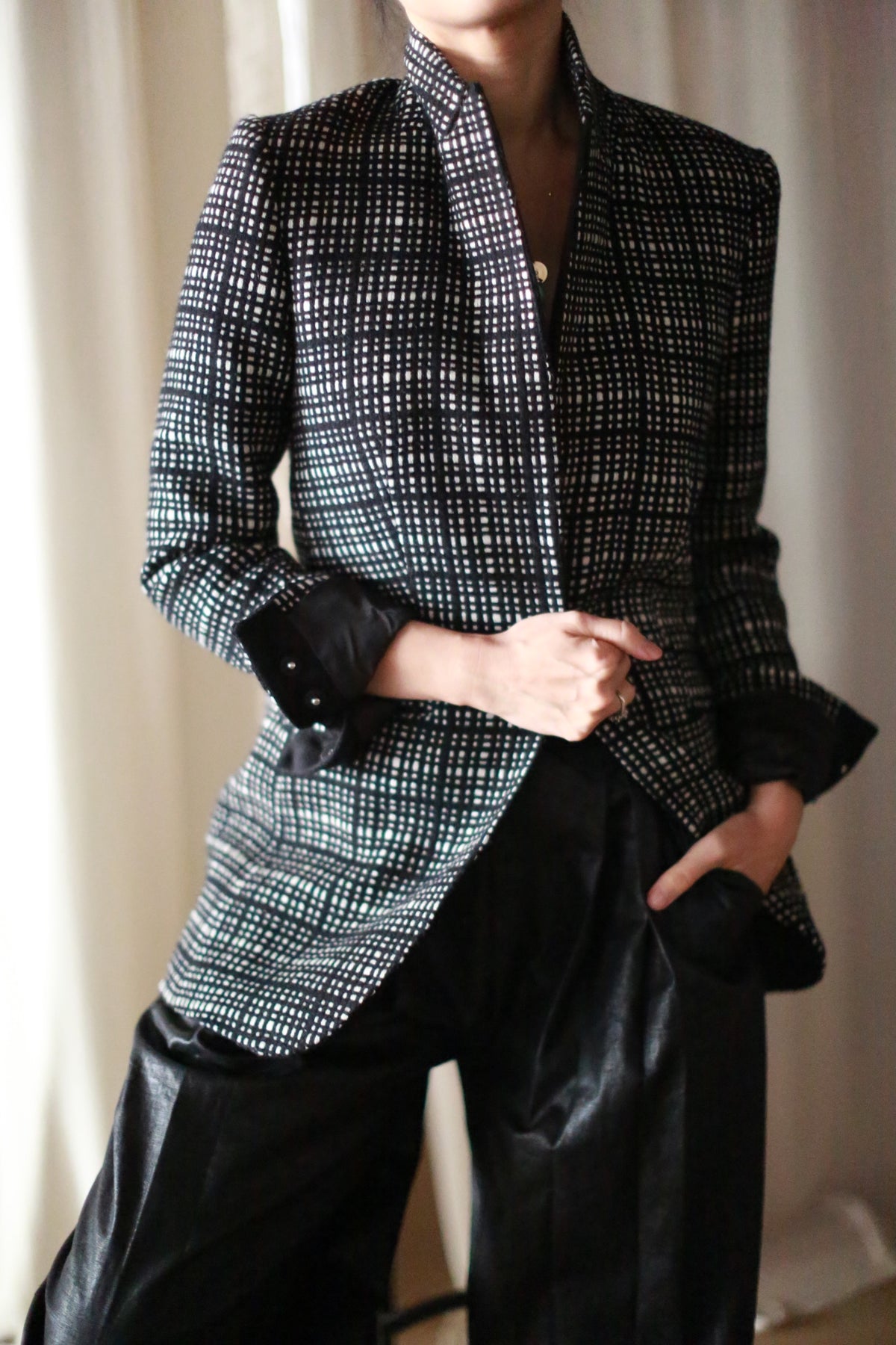 A person wears the Sloane | Plaid black and white cashmere blazer over a black shirt with black pants, standing with one hand in their pocket and the other holding the blazer, set against a softly lit neutral background.