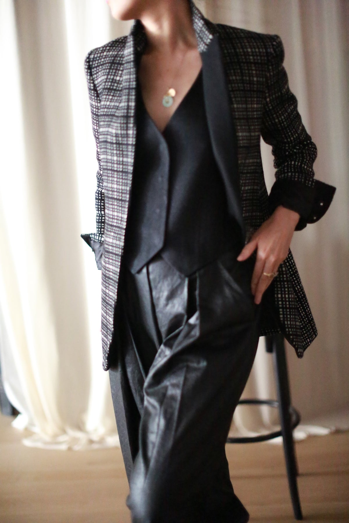 Wearing the Sloane | Plaid cashmere blazer inspired by men’s tailoring, a person in a black top and high-waisted pants stands with one hand in their pocket and the other on their hip against a softly lit neutral backdrop.
