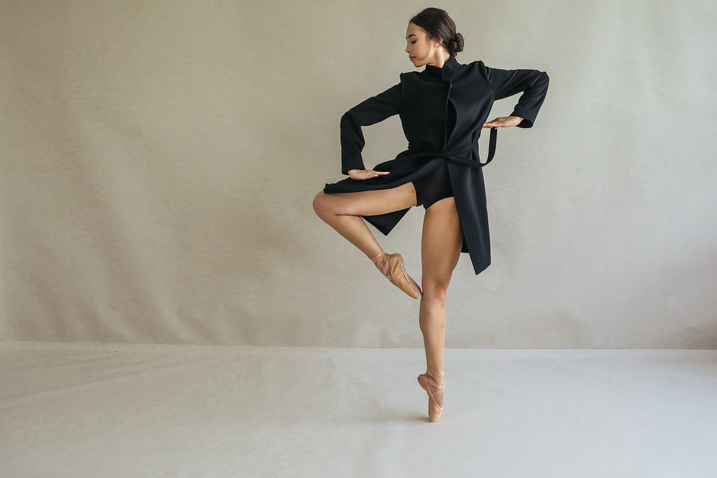 A dancer in black, wearing the reversible cashmere collar "Edmonton," gracefully poses on one leg against a neutral background with elegantly positioned arms and her hair styled in a bun.