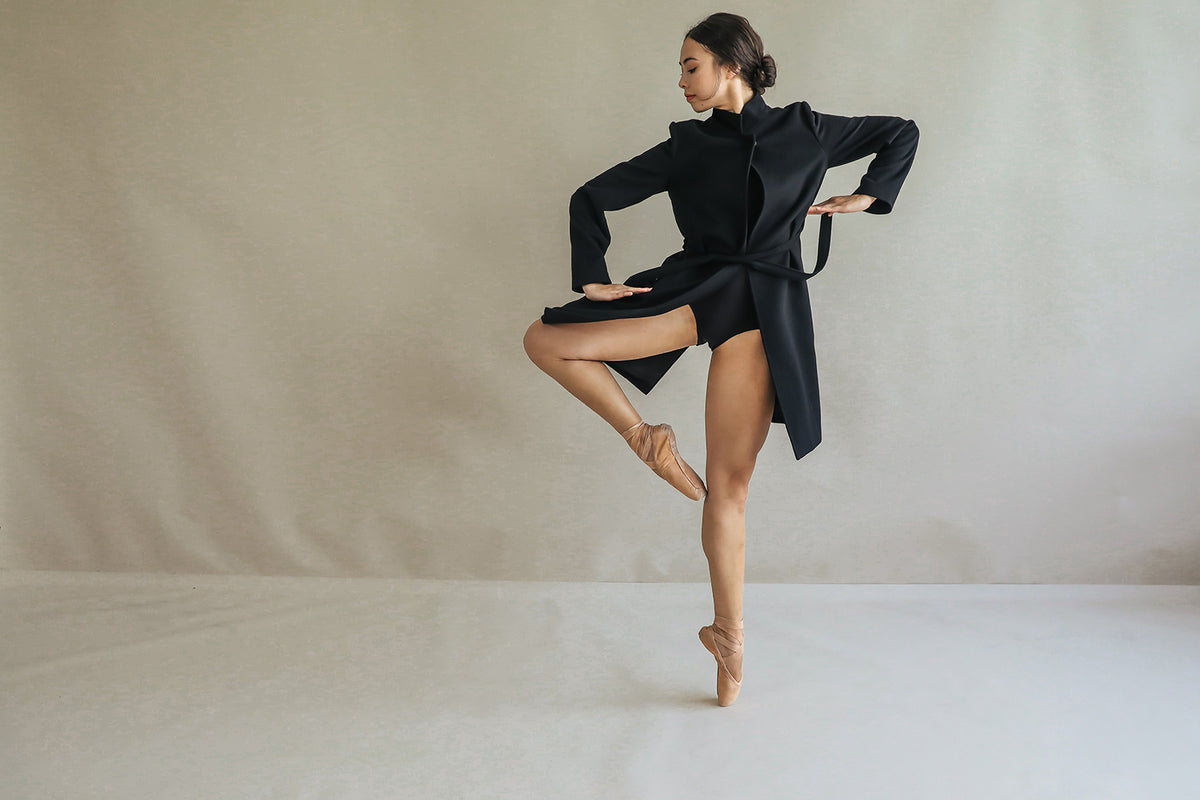 A dancer in black, wearing the reversible cashmere collar "Edmonton," gracefully poses on one leg against a neutral background with elegantly positioned arms and her hair styled in a bun.
