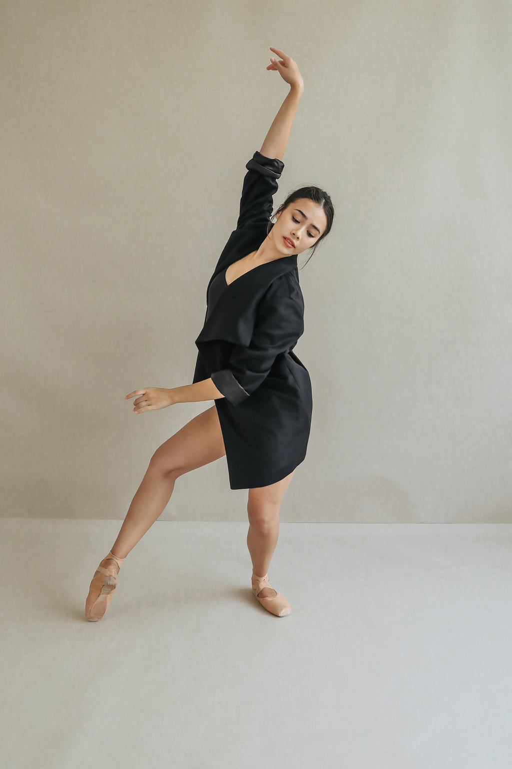A ballet dancer showcases the relaxed fit Winston draped-collar jacket and pink pointe shoes, posing gracefully on one foot with an arm raised against a plain light-colored background.