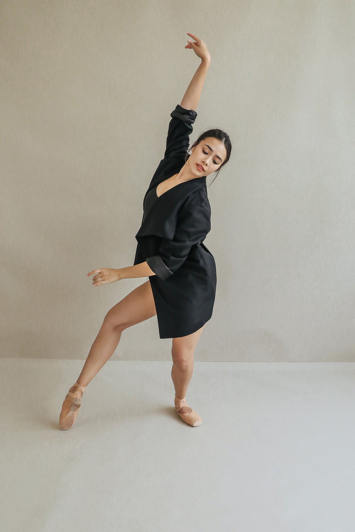 A ballet dancer showcases the relaxed fit Winston draped-collar jacket and pink pointe shoes, posing gracefully on one foot with an arm raised against a plain light-colored background.
