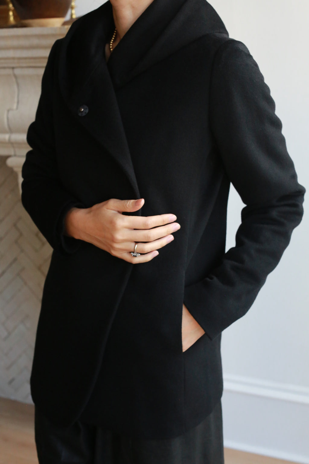 A person wearing the Mitchley jacket stands indoors, upper body visible, with one hand holding the coat closed and the other in a pocket.